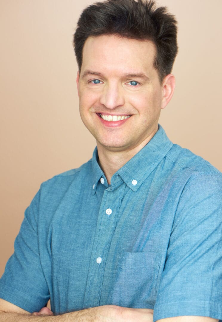 Smiling man in a blue button-up shirt with arms crossed.