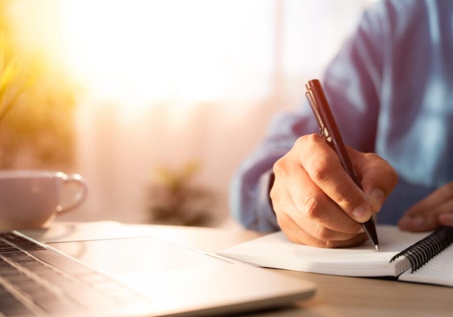 Person writing notes near a laptop.